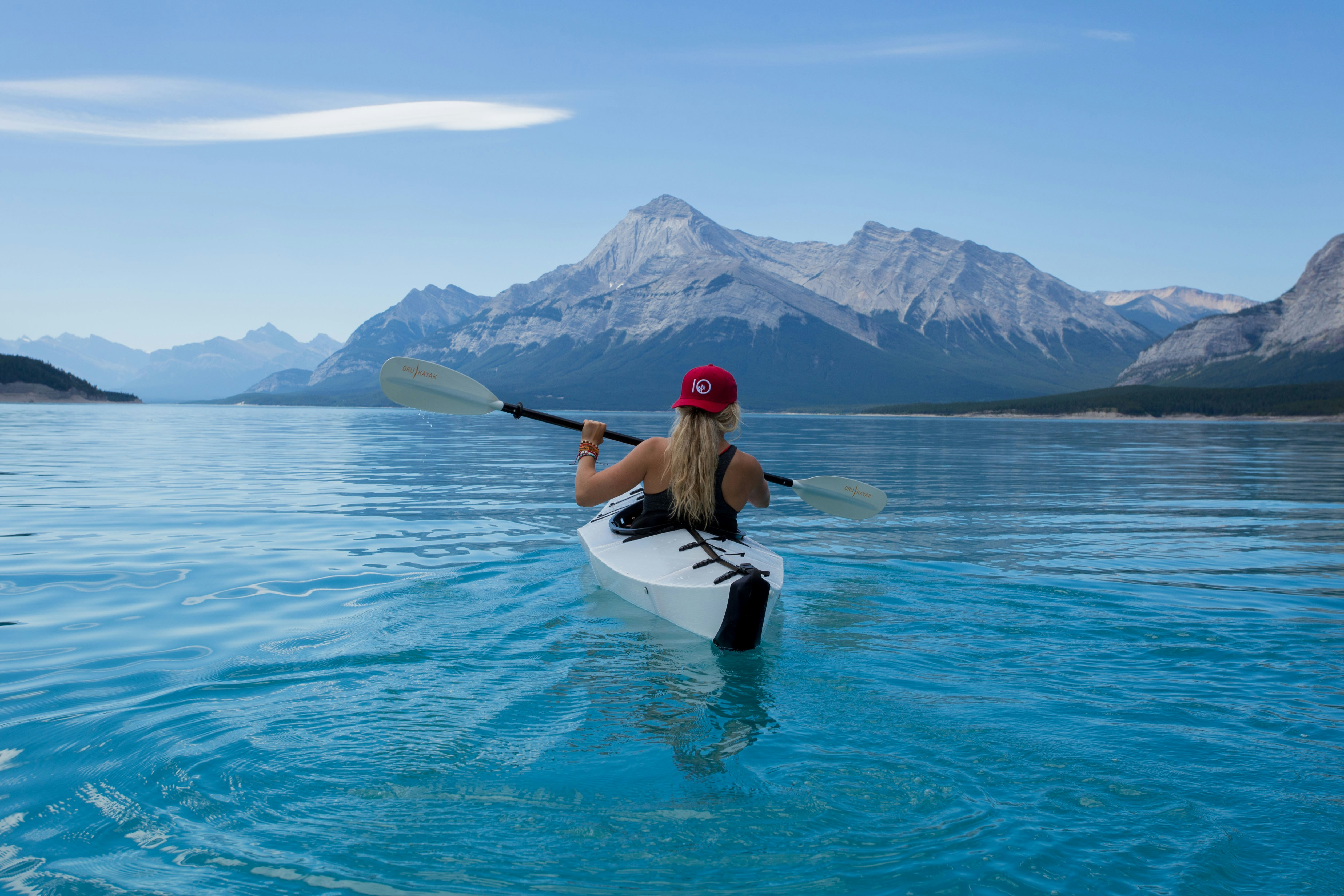 woman wearing red hat riding on white kayak facing mountain alps